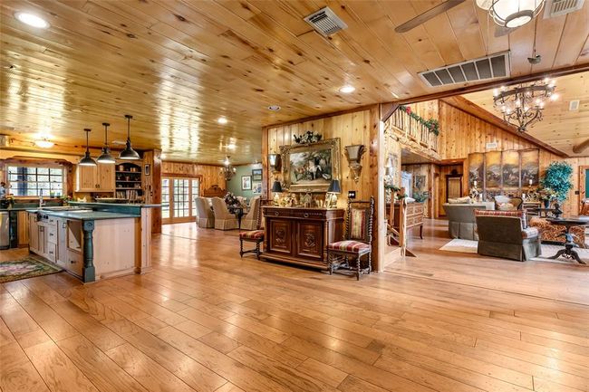 This spacious, rustic home features a warm, open-concept living area with wooden floors and ceilings. The kitchen is equipped with a large island and pendant lighting, while the adjoining dining and living spaces offer cozy seating and elegant decor. The abundant wood finishes create a welcoming, cabin-like atmosphere. | Image 21