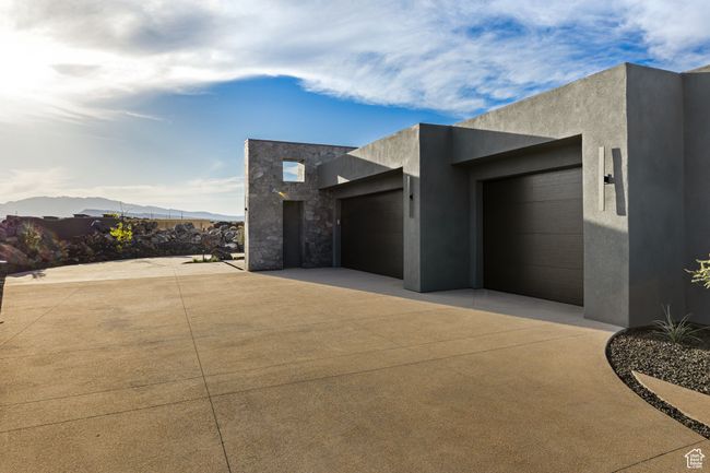 View of side of home featuring an attached garage, stone siding, concrete driveway, and stucco siding | Image 17