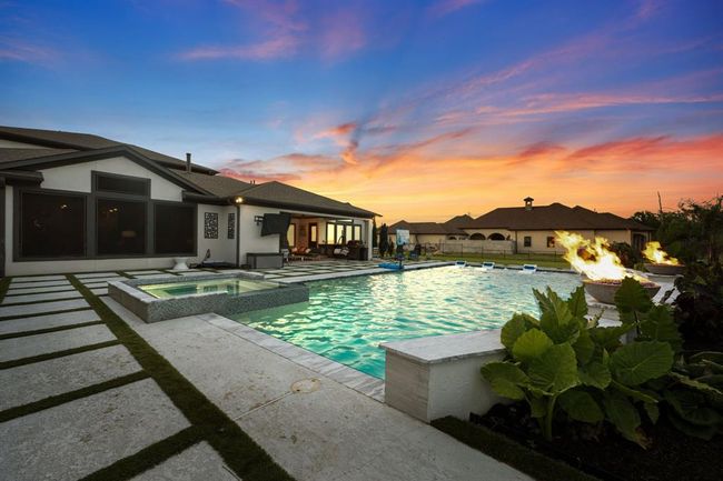 This stunning property features a luxurious outdoor living space with a sparkling pool, hot tub, and fire features. The modern home has large windows and a spacious patio, perfect for entertaining against a picturesque sunset backdrop. | Image 46