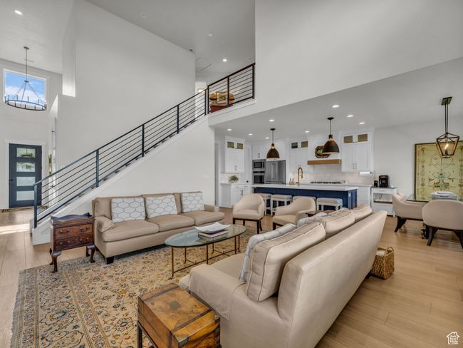 Living room with a towering ceiling, light wood-style floors, a chandelier, recessed lighting, and stairway | Image 9
