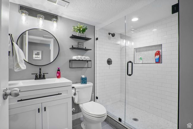 Bathroom featuring visible vents, toilet, vanity, a textured ceiling, and a stall shower | Image 25