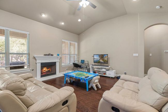 Living area with arched walkways, lofted ceiling, ceiling fan, wood finished floors, and a warm lit fireplace | Image 9