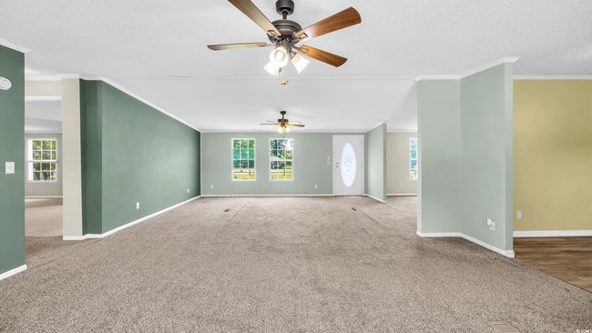 Unfurnished living room featuring a ceiling fan, ornamental molding, carpet, and a textured ceiling | Image 5