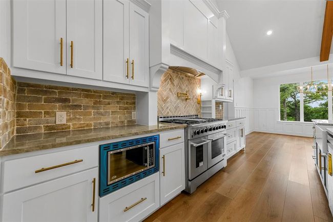 Kitchen featuring light wood-type flooring, tasteful backsplash, white cabinetry, and stainless steel appliances | Image 14