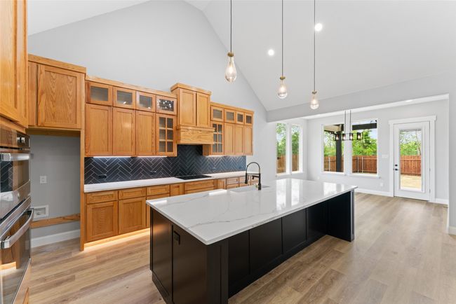 Kitchen featuring light stone countertops, a sink, high vaulted ceiling, backsplash, and pendant lighting | Image 13