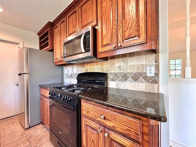Kitchen with appliances with stainless steel finishes, backsplash, light tile patterned flooring, and brown cabinetry | Image 9