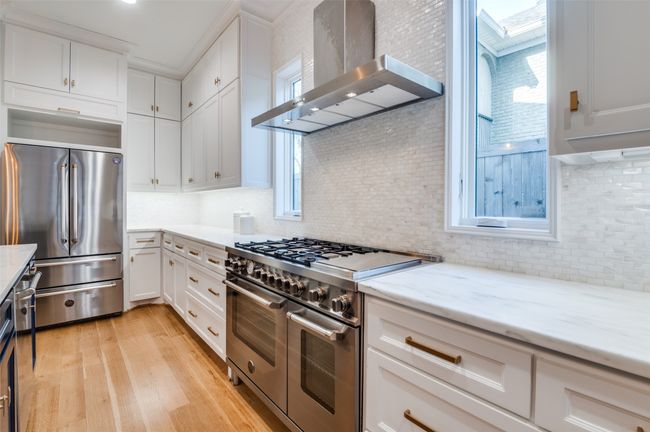 Kitchen with stainless steel appliances, tasteful backsplash, white cabinetry, light wood-style floors, and wall chimney range hood | Image 11