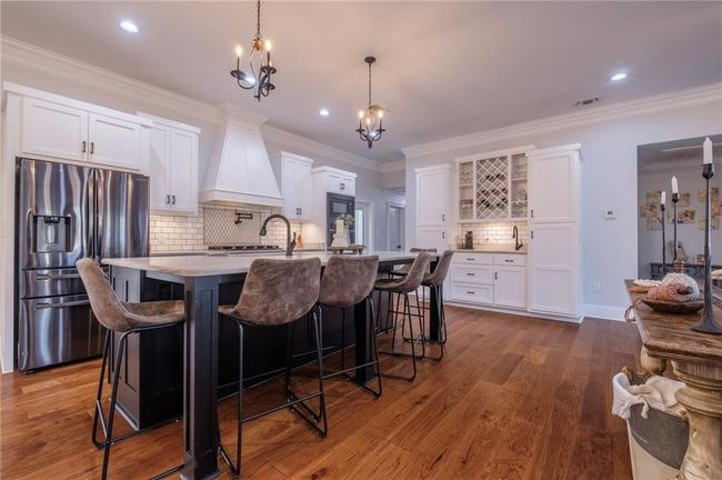 Kitchen with white cabinetry, decorative backsplash, stainless steel fridge, and a center island with sink | Image 12