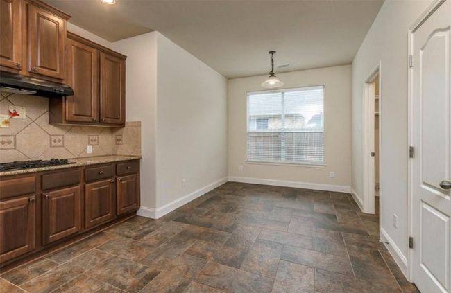 Kitchen with under cabinet range hood, black gas cooktop, baseboards, dark stone finish flooring, and backsplash | Image 7