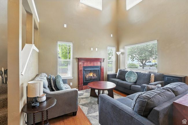Living room with wood finished floors, a tiled fireplace, and a high ceiling | Image 6