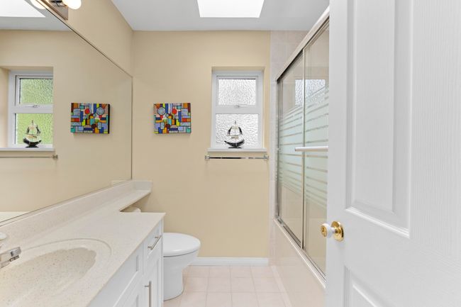 Bathroom with a skylight, vanity, tile patterned floors, and shower / bath combination with glass door | Image 25