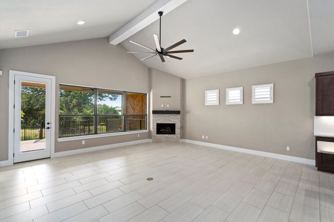 Unfurnished living room featuring ceiling fan, beamed ceiling, high vaulted ceiling, a stone fireplace, and recessed lighting | Image 5