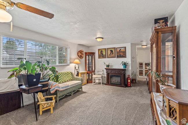 Living area featuring a textured ceiling, ceiling fan, carpet floors, and a fireplace | Image 21
