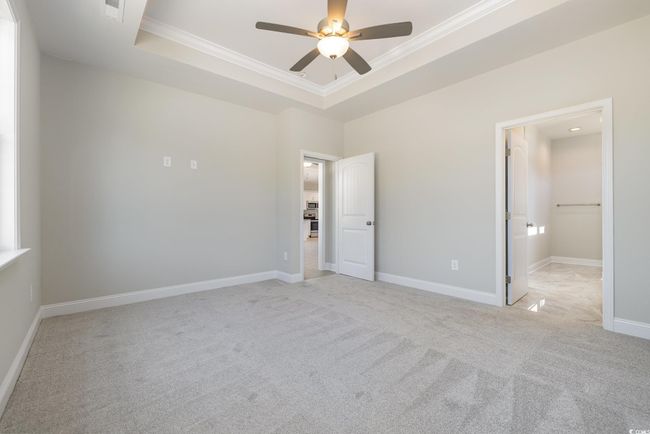 Unfurnished bedroom featuring a tray ceiling, a walk in closet, ceiling fan, and ornamental molding | Image 17