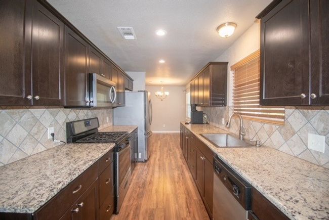 Kitchen with stainless steel appliances, a sink, a chandelier, light wood-style flooring, and baseboards | Image 5