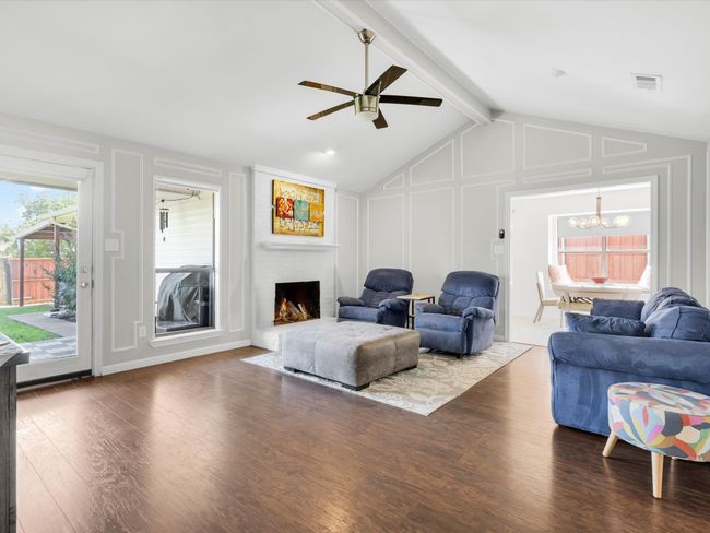 Living area featuring a decorative wall, a ceiling fan, wood finished floors, a fireplace, and a chandelier | Image 11