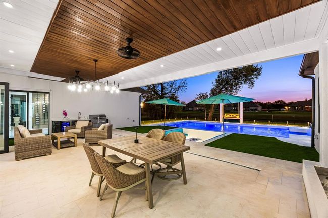 This beautifully designed outdoor living space seamlessly blends luxury and comfort, featuring a spacious covered patio with a stunning wood-paneled ceiling, integrated lighting, and a fully equipped outdoor kitchen perfect for al fresco dining. Enjoy resort-style relaxation beside a pristine, illuminated pool with a built-in spa and sleek water features. The thoughtfully landscaped yard and expansive views create an ideal backdrop for entertaining or unwinding at sunset. | Image 14