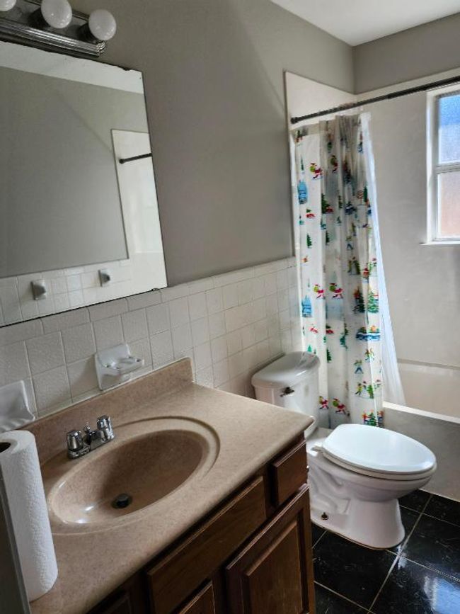 Full bathroom with tile walls, tile patterned flooring, vanity, shower / bath combo with shower curtain, and a wainscoted wall | Image 9