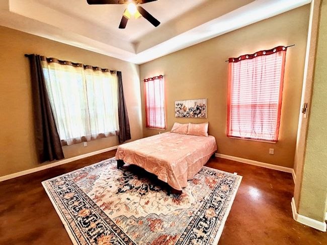 Master Bedroom featuring a tray ceiling, concrete floors, a ceiling fan, and baseboards | Image 8