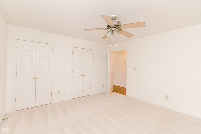 unfurnished bedroom featuring two closets, carpet floors, a ceiling fan, and baseboards | Image 23