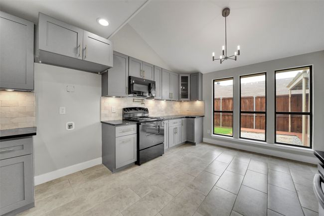 Kitchen with black appliances, gray cabinets, dark countertops, lofted ceiling, and tasteful backsplash | Image 10