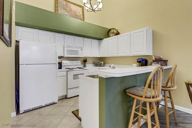 Kitchen with white appliances, a kitchen bar, white cabinets, a high ceiling, and a peninsula | Image 8