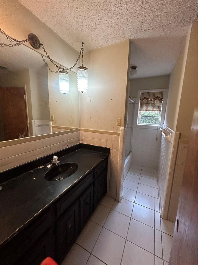 Full bathroom with a textured ceiling, tile patterned flooring, a shower with shower door, a wainscoted wall, and tile walls | Image 18
