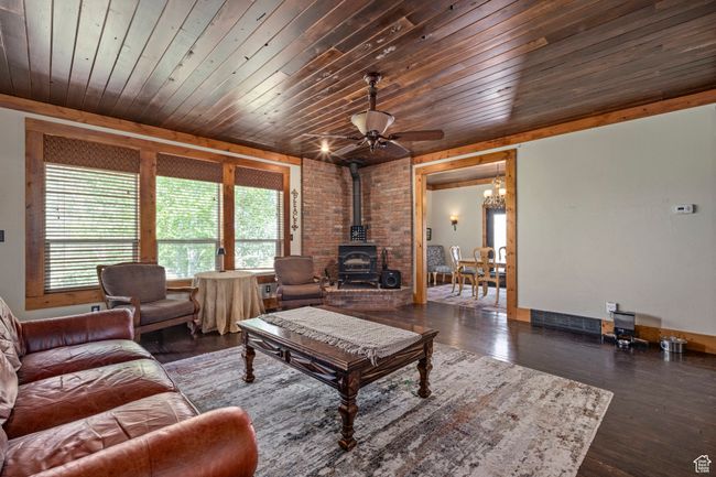 Living area with a wood stove, a ceiling fan, wood finished floors, wood ceiling, and a chandelier | Image 4