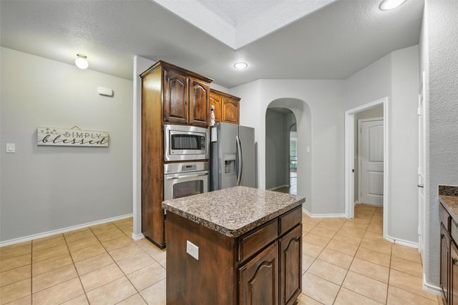 Kitchen with appliances with stainless steel finishes, arched walkways, light tile patterned floors, a center island, and recessed lighting | Image 22