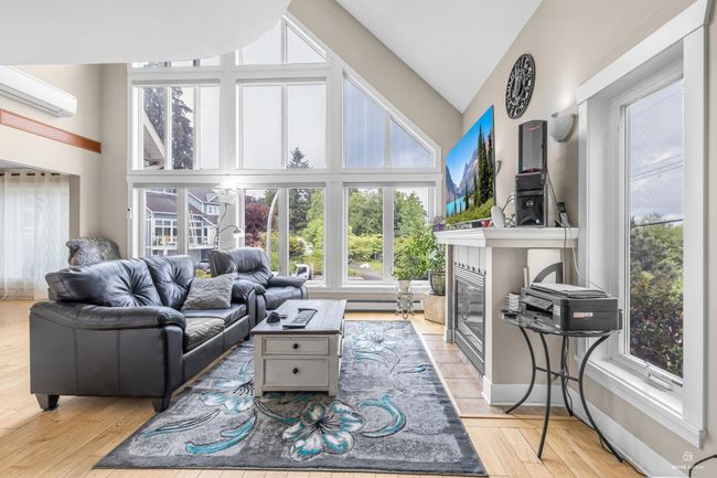 Living area featuring a wall mounted AC, a tile fireplace, high vaulted ceiling, light wood-style flooring, and a baseboard radiator | Image 8