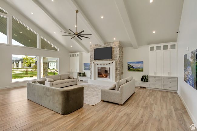 Living room with high vaulted ceiling, a multi sided fireplace, ceiling fan, light wood finished floors, and beamed ceiling | Image 34