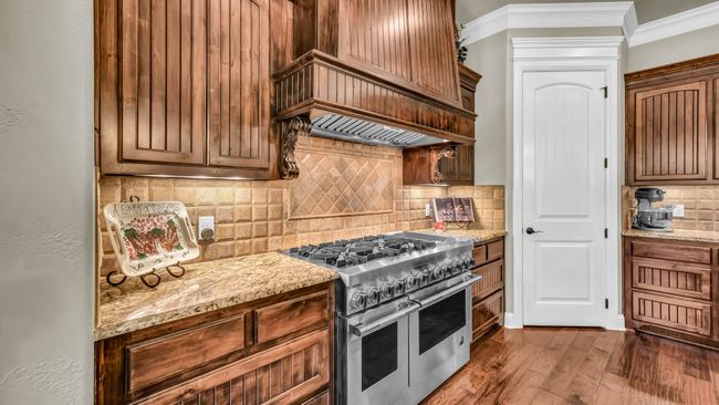 Kitchen featuring double oven range, ornamental molding, tasteful backsplash, wood finished floors, and custom range hood | Image 16