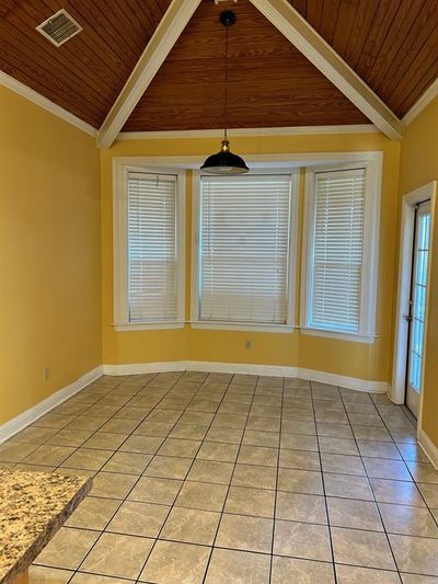 Unfurnished dining area featuring wooden ceiling, light tile patterned floors, vaulted ceiling with beams, and ornamental molding | Image 2