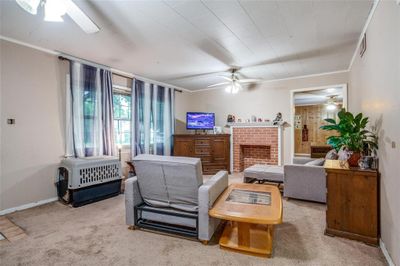 Carpeted living room featuring ceiling fan, crown molding, and a brick fireplace | Image 3