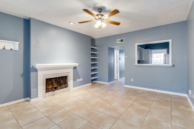Unfurnished living room with ceiling fan, a tile fireplace, a textured ceiling, tile patterned floors, and built in features | Image 7