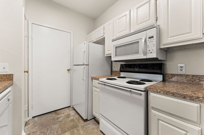 Kitchen featuring dark countertops, white cabinets, white appliances, and stone finish flooring | Image 10