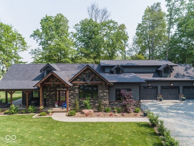 view of front of property with gravel driveway, a front lawn, stone siding, a garage, and roof with shingles | Image 54