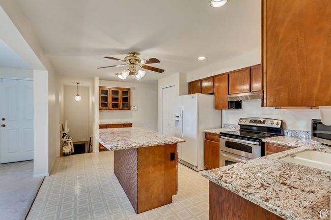 Kitchen featuring stainless steel appliances, light floors, a ceiling fan, light stone countertops, and a kitchen island | Image 6