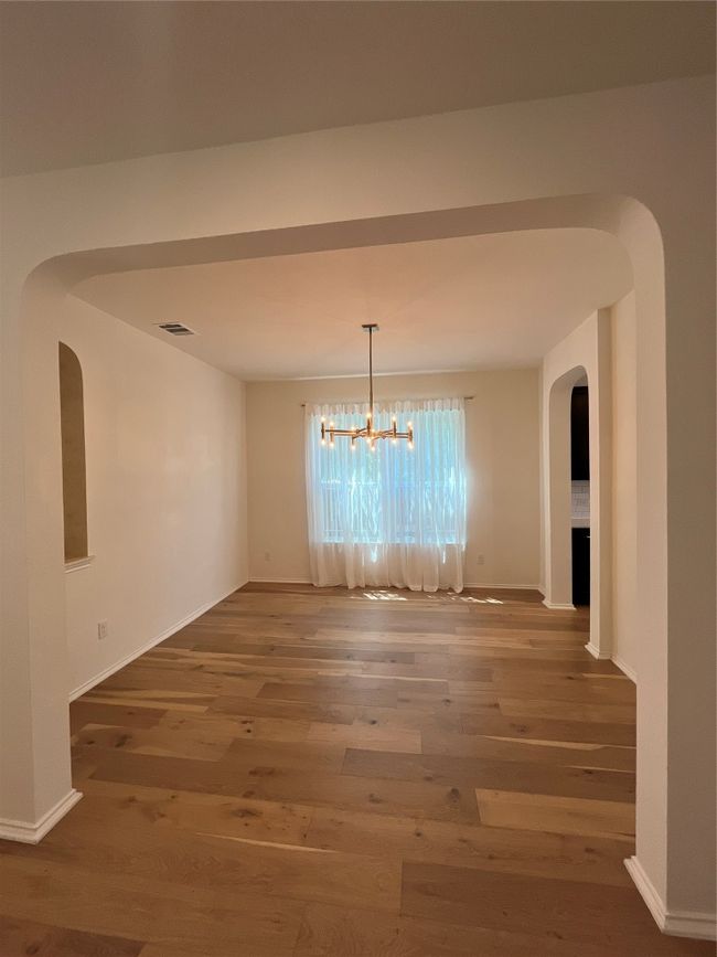 Unfurnished dining area with visible vents, wood finished floors, baseboards, a chandelier, and arched walkways | Image 4