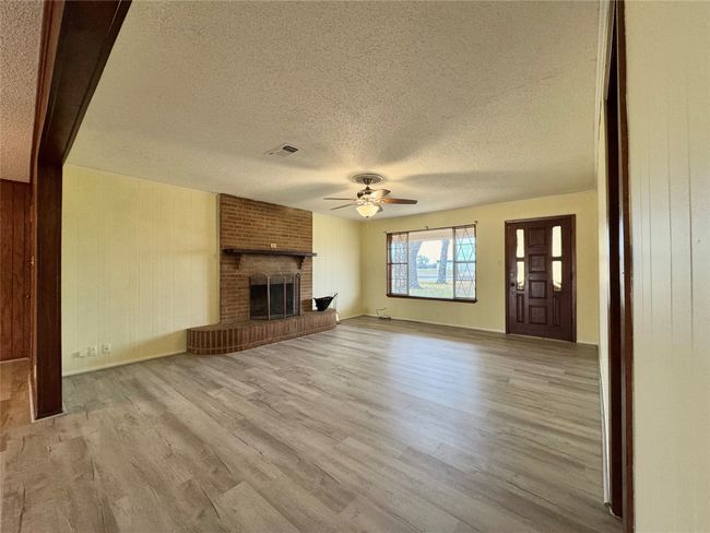 Unfurnished living room featuring a brick fireplace, a textured ceiling, light hardwood / wood-style floors, and ceiling fan | Image 14
