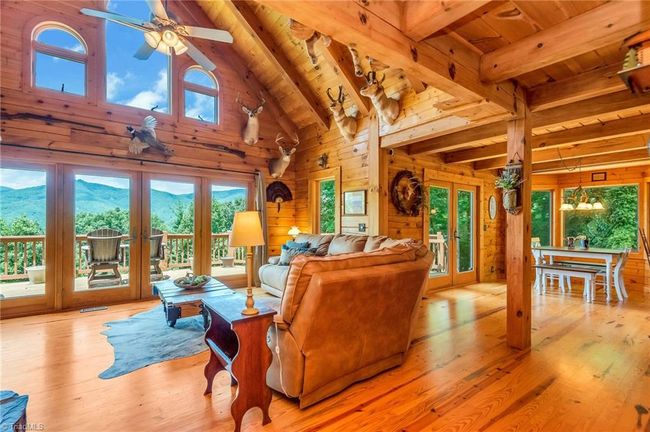 The large open-concept dining room and kitchen in the rustic cabin feature a bay window, expansive long-range views, seamlessly connecting to a wrap-around deck ideal for entertaining and outdoor BBQs, blending indoor comfort with scenic outdoor enjoyment. | Image 19