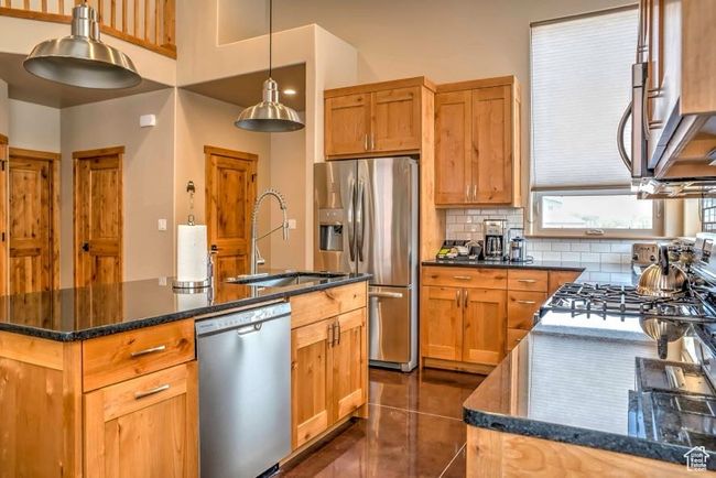 Kitchen featuring stainless steel appliances, a sink, tasteful backsplash, a kitchen island with sink, and dark tile patterned floors | Image 7