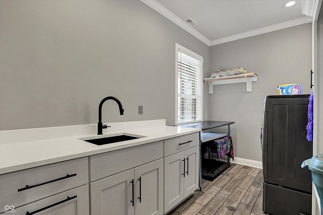 clothes washing area featuring wood tiled floor, visible vents, ornamental molding, a sink, and baseboards | Image 17