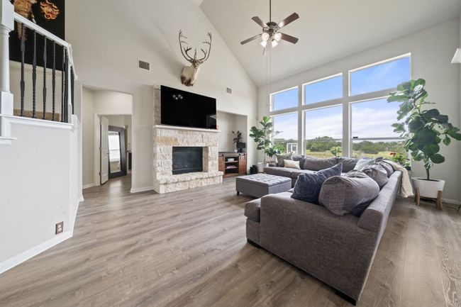 Living room with high vaulted ceiling, a stone fireplace, ceiling fan, and wood finished floors | Image 6