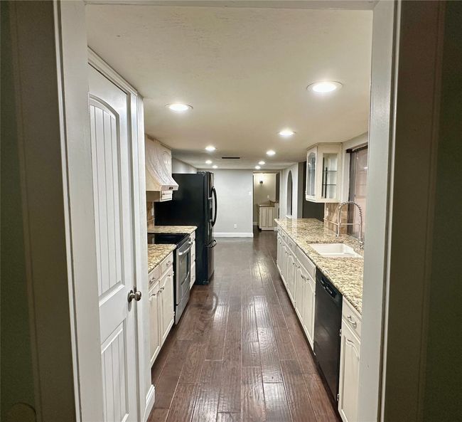 Kitchen with recessed lighting, black appliances, dark wood-style flooring, glass insert cabinets, and light stone countertops | Image 14