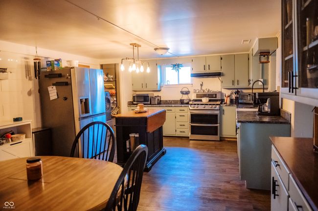 kitchen featuring appliances with stainless steel finishes, under cabinet range hood, dark countertops, hanging light fixtures, and dark wood-style floors | Image 21