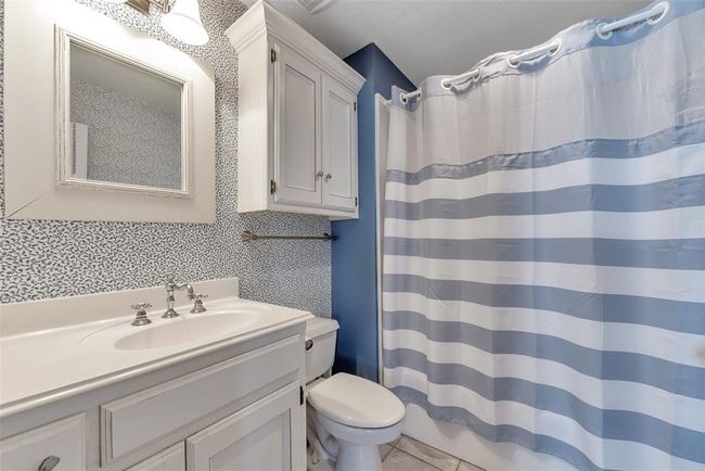 Full bath features a classic tub/shower combo, tile flooring, and linen cabinetry for extra storage. Clean, coastal, and ready for everyday comfort or guest use. | Image 19