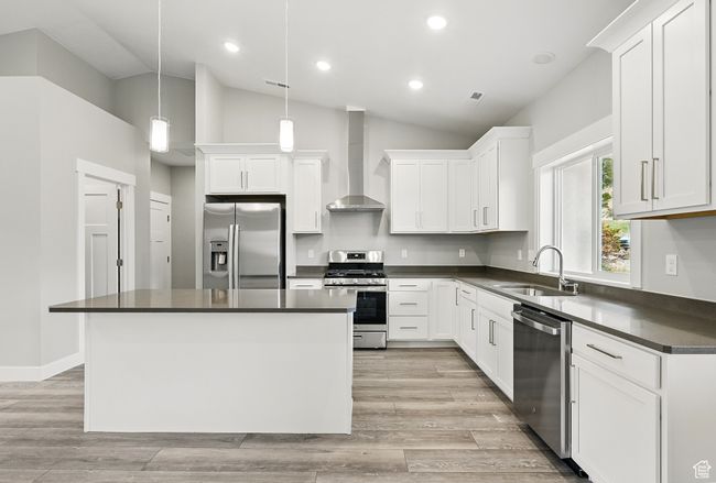 Kitchen featuring stainless steel appliances, wall chimney range hood, a sink, dark countertops, and vaulted ceiling | Image 18