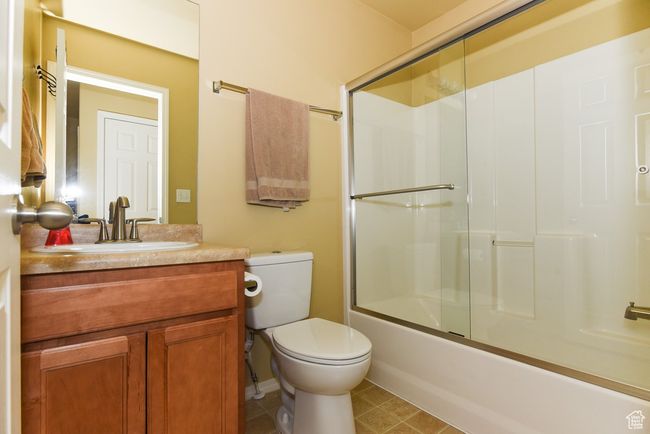 Full bathroom featuring toilet, tile patterned floors, bath / shower combo with glass door, and vanity | Image 26