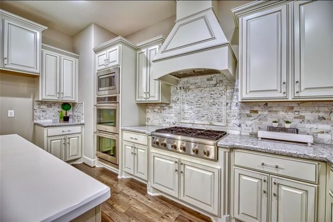 This kitchen features elegant white cabinetry, granite countertops, and a stylish marble backsplash. It includes a modern stainless steel range and double oven, with ample storage and a bright, open layout. | Image 22